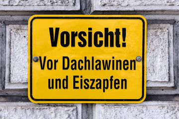 Germany: Yellow warning sign on an exterior wall: Watch out! Roof avalanche and icicles (Vorsicht! Dachlawinen und Eiszapfen) - concept danger winter ice frost snow hazard risk advice information