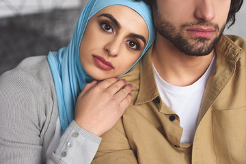 attractive muslim girlfriend in hijab leaning on boyfriends shoulder at home