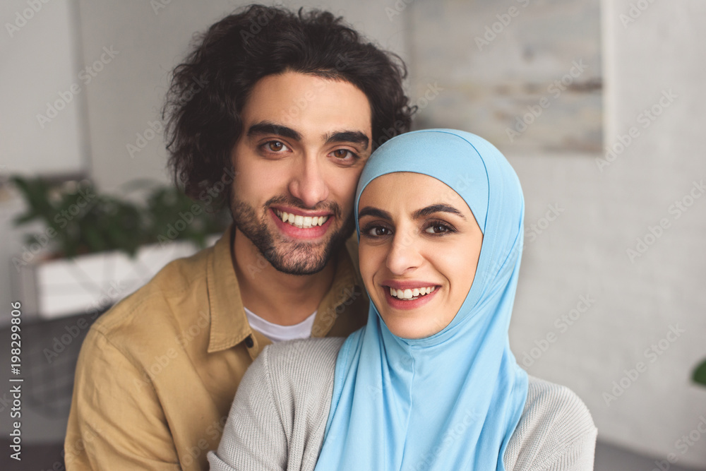 Sticker portrait of smiling muslim couple looking at camera at home