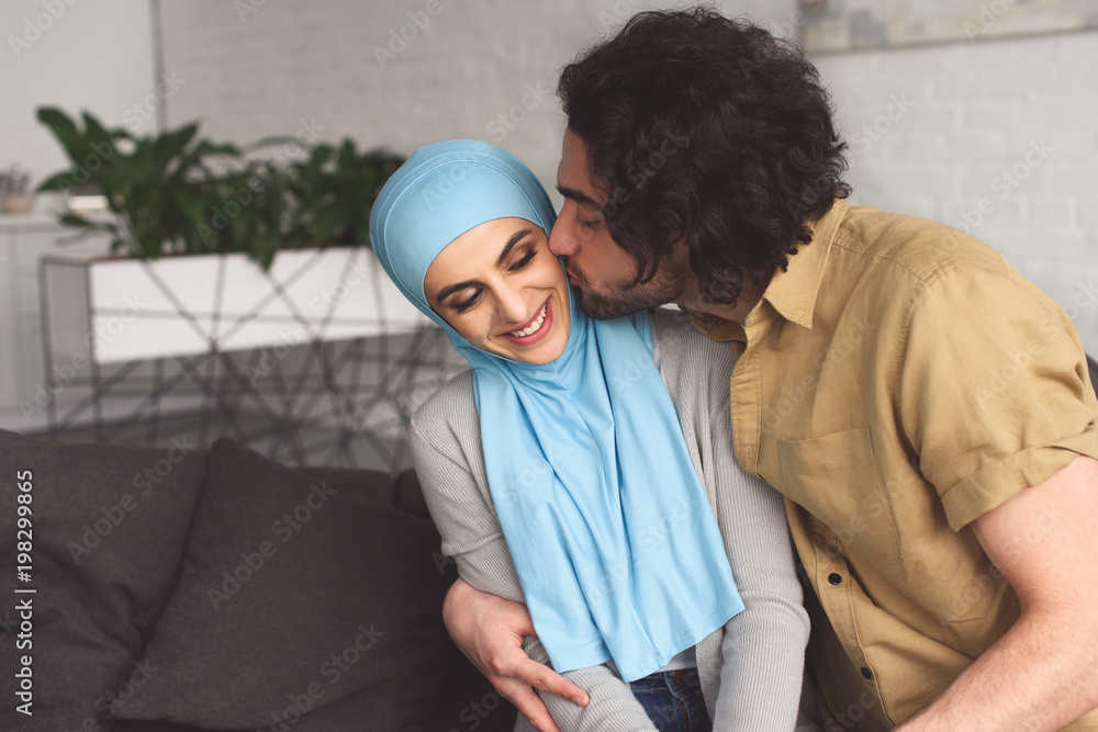 Wall mural muslim boyfriend kissing girlfriend in hijab at home