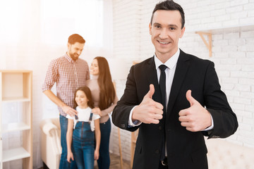 Happy man in suit shows thumbs up. House for sale. Young family looks at apartments.