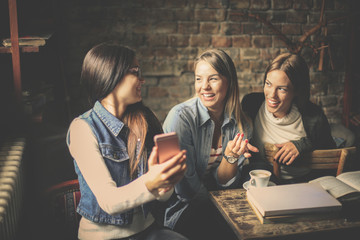 Three students girls having conversation and using smart phone.