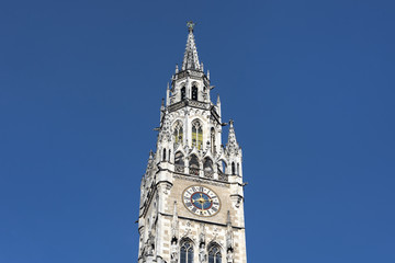 Fototapeta na wymiar Germany, Bavaria, Munich, Marienplatz: Front view detail of famous clock tower of the New Town Hall (Neues Rathaus) in the city center of the Bavarian capital with blue sky in the background.