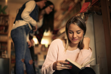 Young student girl sitting in library and reading book.