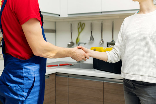 plumber and woman shaking hands after repairs at home kitchen