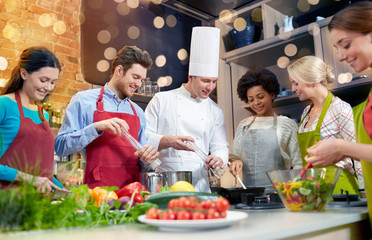 cooking class, culinary, food and people concept - happy group of friends and male chef cook...