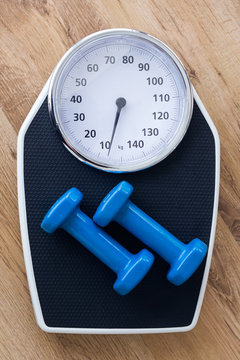 Blue dumbbells on top of weight scale on wooden background in the gym.