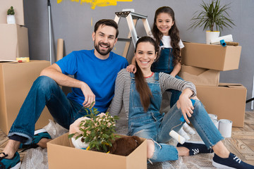 Happy young family dismantles cardboard boxes and makes repairs in new house.