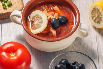 Soup saltwort with meat, potatoes, tomatoes, lemon, black olives and sour cream in ceramic soup bowl