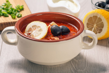 Soup saltwort with meat, potatoes, tomatoes, lemon, black olives and sour cream in ceramic soup bowl