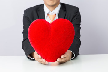 Businessman holds out the  red heart, isolated background
