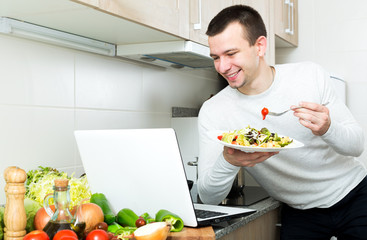 Successful man tasting vegetables dish near laptop