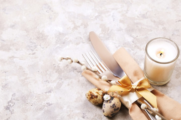 Easter table setting composition: fork, knife candle, wildflowers, pussy willow on plate w/ napkin, white stucco plaster texture background. Close up, top view, copy space