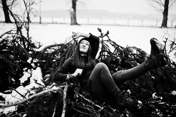 Young girl wear on long green sweatshirt, jeans and black headwear at  branches of the pine tree in winter day.