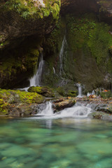 Fototapeta na wymiar Smoll waterfall among rocks covered with green moss