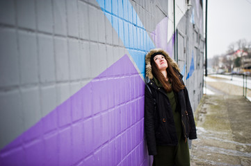 Young girl posed against colored wall in cold day.