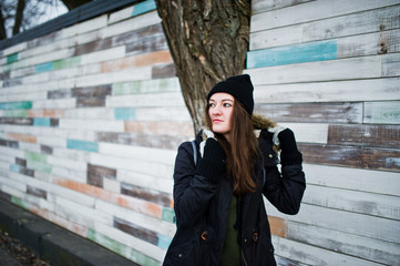 Young girl wear black headwear against wooden wall.