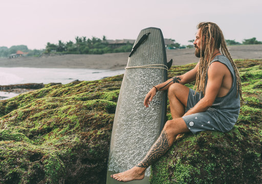 Surfer man with dreadlocks, tattoos near ocean