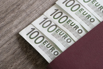 Passport with one hundred Euro banknotes entered into passport page on wooden background