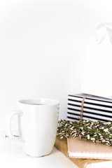 Lifestyle composition with mug, greenery and gold notebooks, gift bag on white background