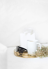 Lifestyle composition with mug, greenery and gold notebooks, gift bag, gold tray on white background