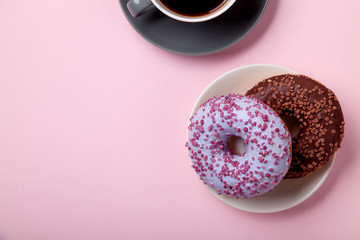 Glazed berry and chocolate donuts with sweet sprinkles on pink background with a cup of black coffee