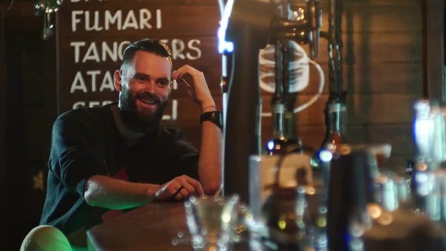 Bearded guy drinks a cocktail and communicates with the bartender at the bar counter in 4k resolution in slow motion