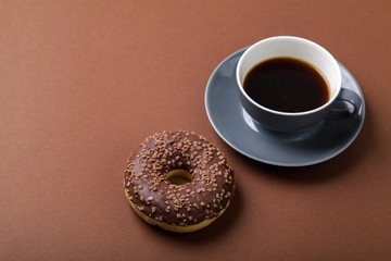 Chocolate donut and cup of black coffee on brown background. Monochromatic concept.