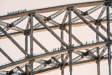 Tourists climb on two layers of the Sydney Harbour Bridge. The sun is catching the bottom of the...