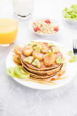 Homemade breakfast on a marble grey table. Stack of pancakes with a grilled bananas and a caramel. Glass of juice, orange, kiwi slices.Healthy breakfast concept, flat lay, top view