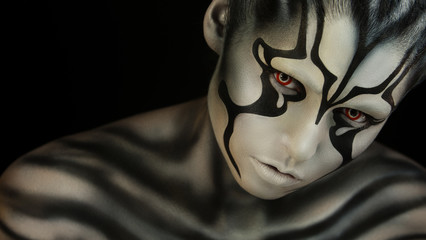 Watchfully looking and  intently looking after.Creative appearance of alien creature with red  eyes and black and white skin is created through a make-up and body-art