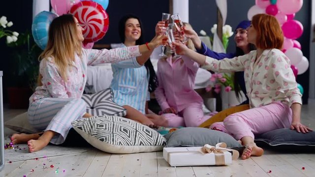 A group of dancing girls at a pajama party with glasses of champagne laugh and smile. The bachelorette party is in full swing. Beautiful women sit in a circle and discuss fashion trends