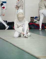 Fencer in white costume with rapier and protective mask ties shoelaces