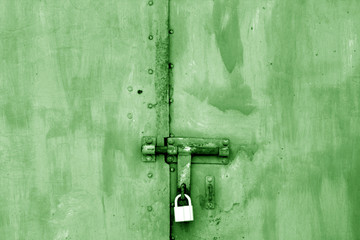 Old padlock on metal gate in green tone.