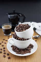 Espresso shot, coffee beans in the cup and coffee percolator on wooden table with black background