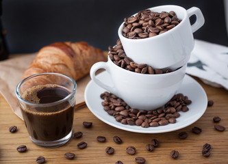 Espresso shot, coffee beans in the cup and croissant on wooden table with black background