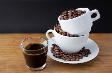 Espresso shot and coffee beans in the cup on wooden table with black background