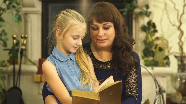 Happy young mother with her little smiling daughter reading the bood together - indoors