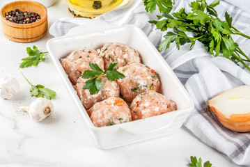 Raw homemade chicken or turkey meatballs in baking dish on white marble background. Copy space.