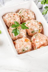Raw homemade chicken or turkey meatballs in baking dish on white marble background. Copy space.