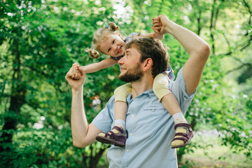 Obraz premium Father and daughter playing piggyback at outdoor garden park. Cute little blonde girl and man with a beard having fun