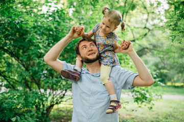 Father and daughter playing piggyback at outdoor garden park. Cute little blonde girl and man with a beard having fun