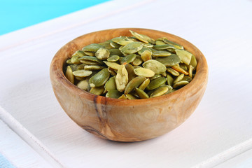 Full bowl of pumpkin seeds close up on a wooden table.