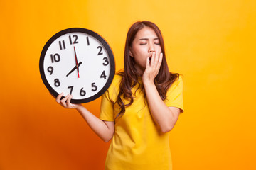 Sleepy young Asian woman with a clock in the morning in yellow dress