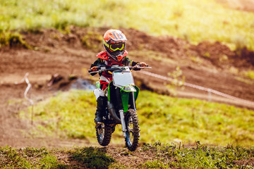 Racer child on motorcycle participates in motocross cross-country in flight, jumps and takes off on springboard against sky. Concept active extreme rest teenager. © Parilov