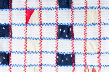 Textile pattern of square pieces of colored fabrics, sewn by red and blue zigzag seams on white...