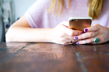 A young girl is sitting at the table and looking into her smartphone. Close-up of hands model with smartphone. Close up view with copy space