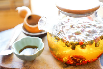 Chinese green tea in a transparent teapot is on a wooden table. In the background, a bright sunny...