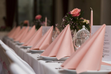 Wedding table with white tablecloth, chairs, pink napkin, plates and dishes