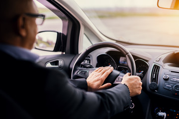 Mature professional elegant businessman in a suit is driving a car and honking.